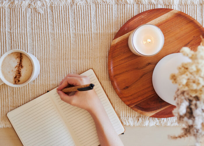 Coffee, hand and writing in journal top view with candle for calm, peace and relax morning routine. Woman, notebook and diary planning goals, lifestyle motivation or creative writer with warm drink
